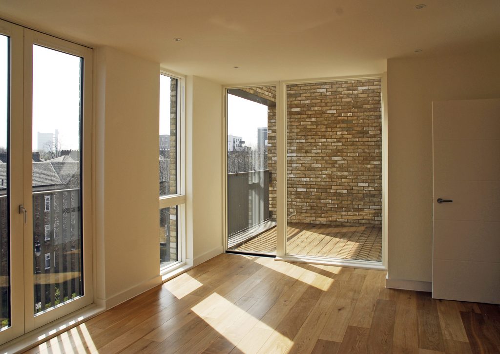 Innenansicht mit Ausblick aus großen rechteckigen Fenstern, die von der Decke bis zum Boden reichen, auf Außenraum und Steinmauer