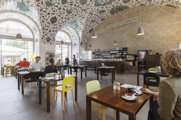 Cafe restaurant with wooden tables and partly colourful chairs and turquoise-white ornamental tiled ceiling