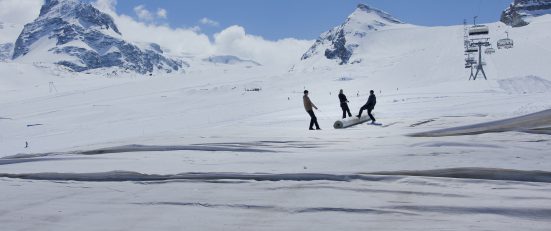 3 people on a snow-covered high alpine landscape pulling a roller together
