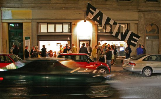 several people in front of a pub, some cars and a flag with the inscription ‘Fahne’ in front of it