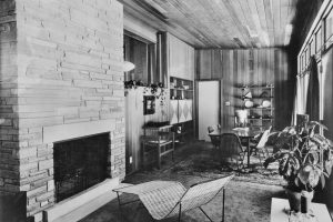 b/w photo of interior with plant, fireplace, deckchair and dining table