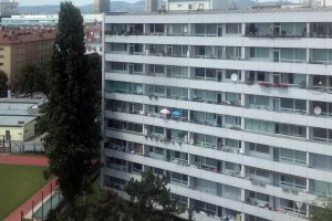 9-stöckiges Hochhaus mit einem Sportplatz links daneben und einer Wiese davor