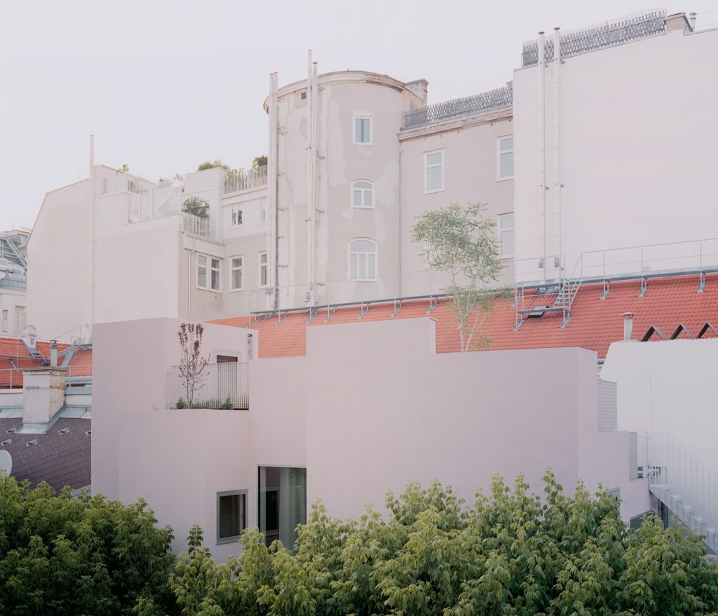 Häuserfassade in sehr hellem rosa mit Bäumen im Vordergrund