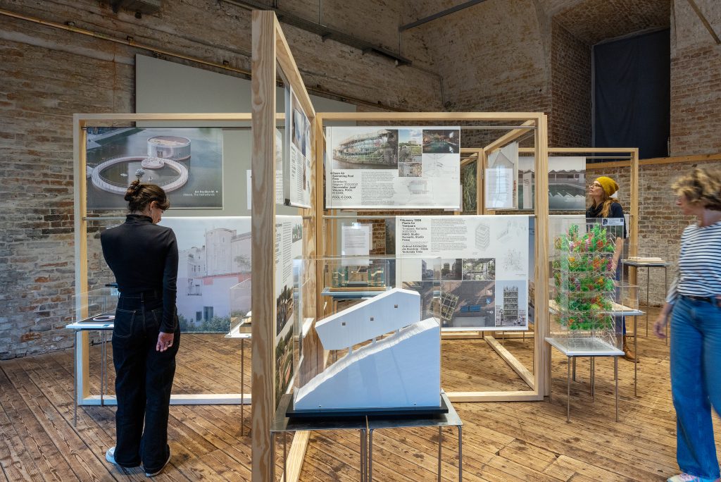 Exhibition room with wooden panels, tables, models, photos and plans on display