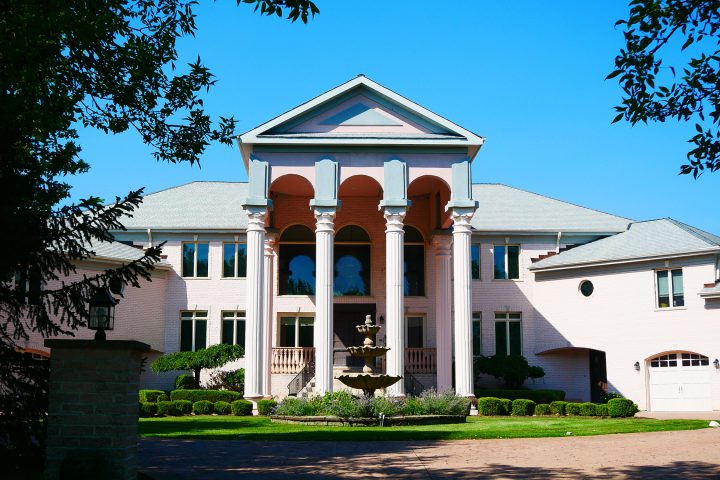 huge house with 4 pillars and a fountain in front of it